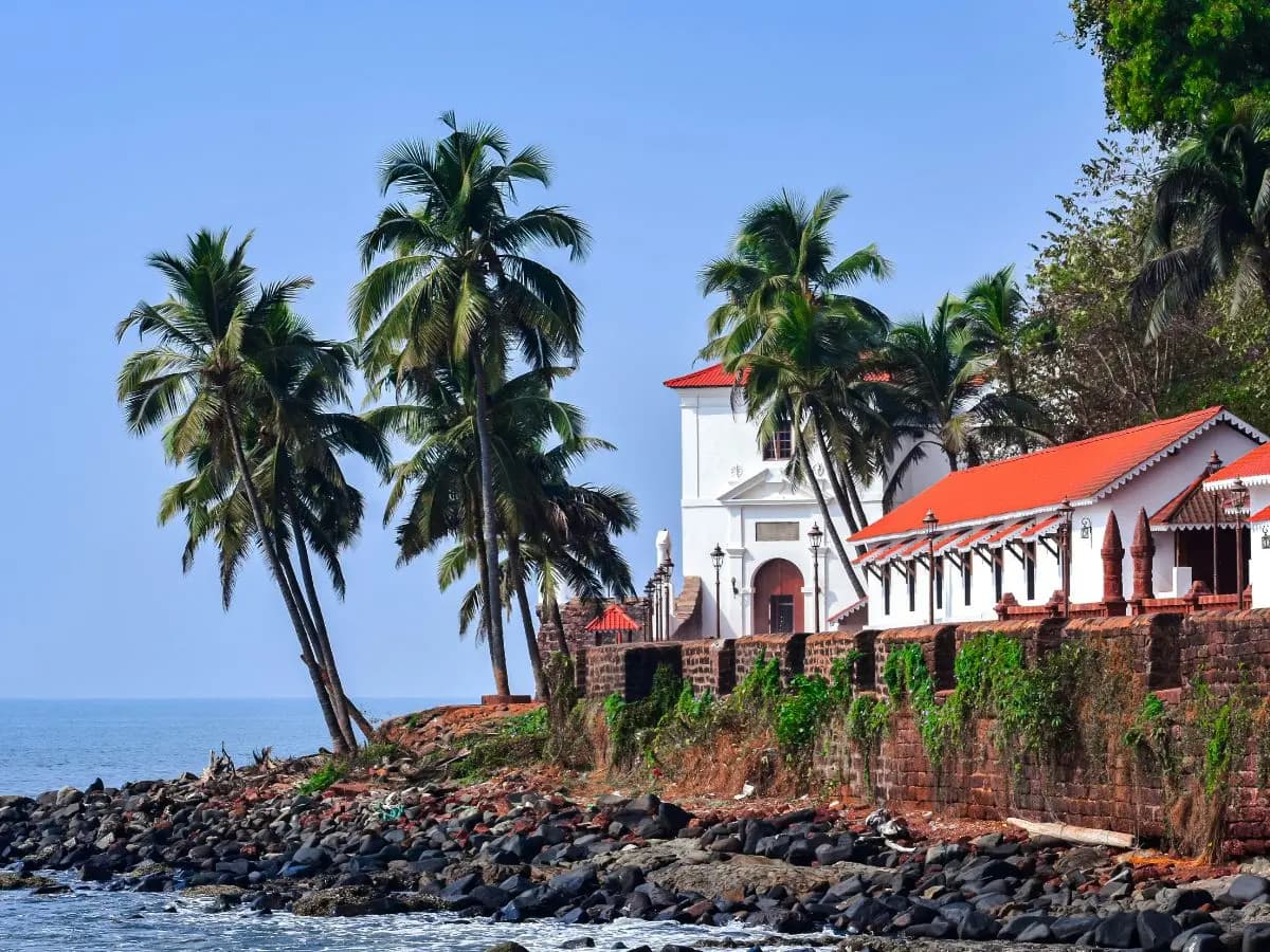 A white Portuguese-era building with a red tile roof behind a laterite wall on the Goan coast