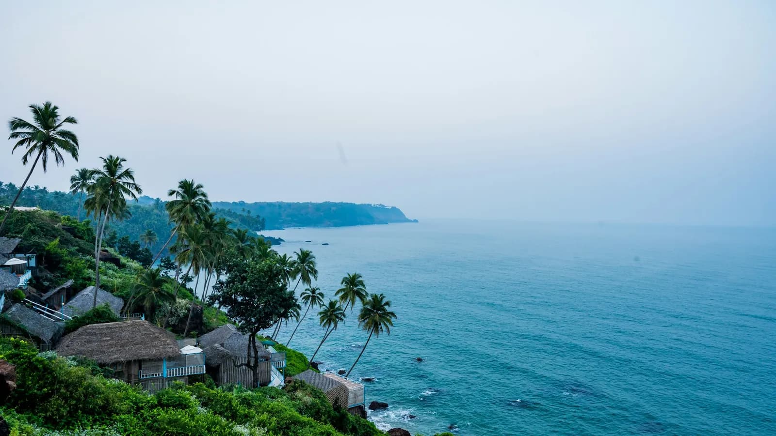Thatched buildings on a green headland above the sea on the Goan coast